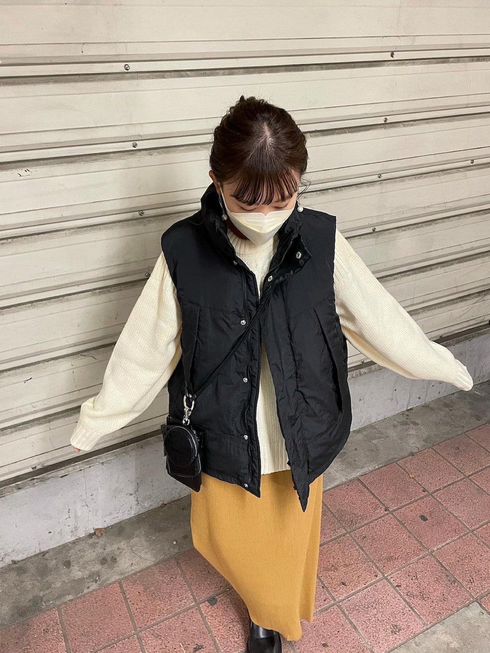 ホワイト系のニット/セーター、ブラック系のダウンベスト、イエロー系のスカートを着用したレディースの秋コーディネートの2枚目の写真