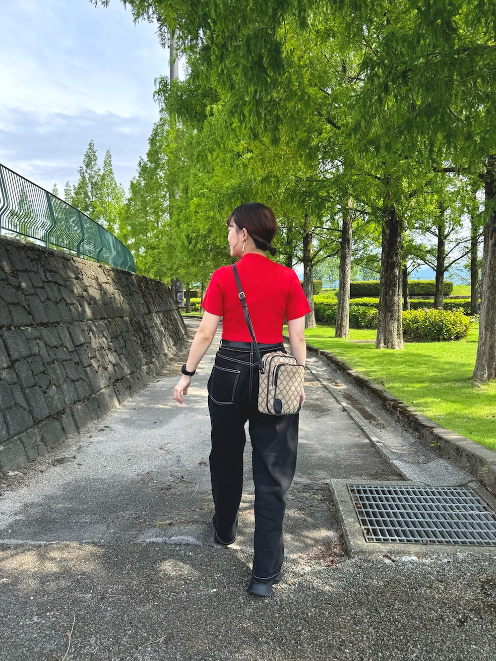 ブラック系のデニムパンツ、レッド系のトップス、ブラック系のショルダーバッグを着用したレディースの夏コーディネートの2枚目の写真