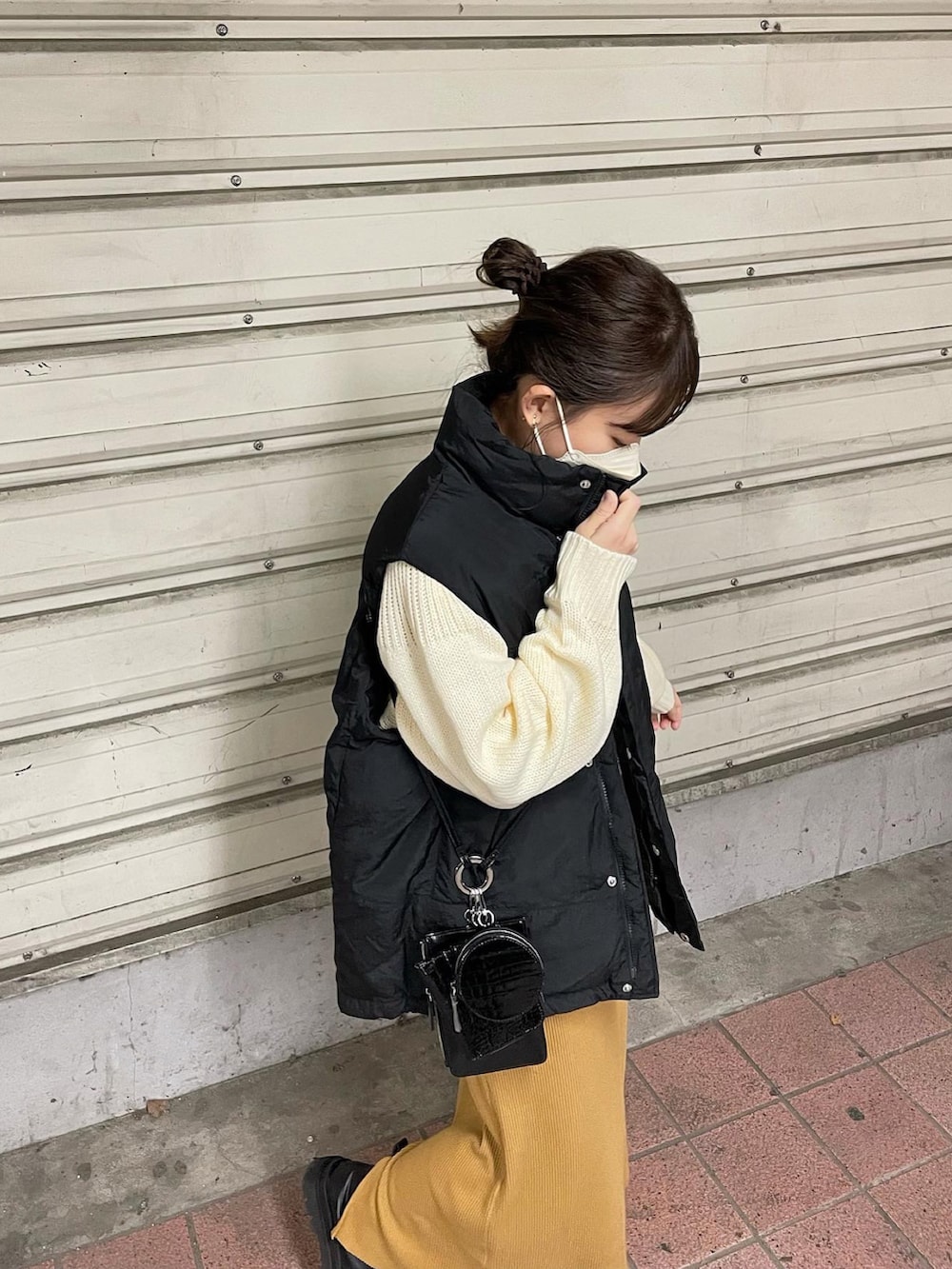 ホワイト系のニット/セーター、ブラック系のダウンベスト、イエロー系のスカートを着用したレディースの秋コーディネートの4枚目の写真