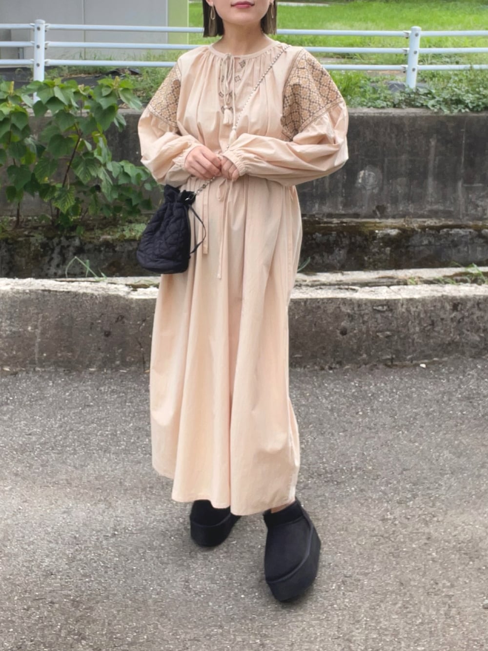 ベージュ系のワンピース、ブラック系のショルダーバッグ、ブラック系のブーツを着用したレディースの秋コーディネートの2枚目の写真