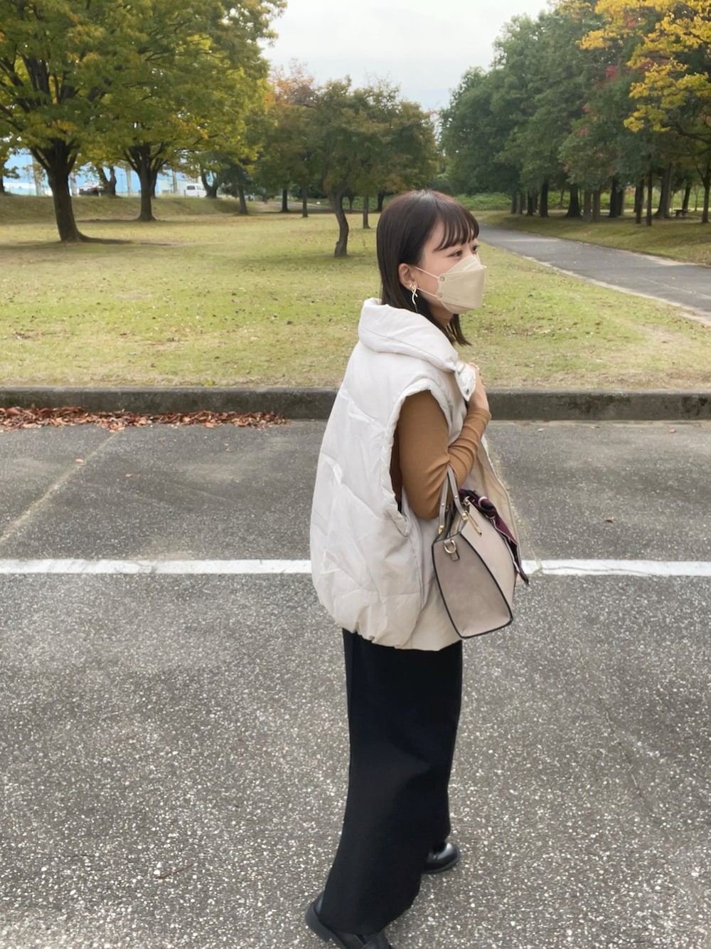 ベージュ系のバッグ、ホワイト系のダウンベスト、イエロー系のトップスを着用したレディースの秋コーディネートの4枚目の写真