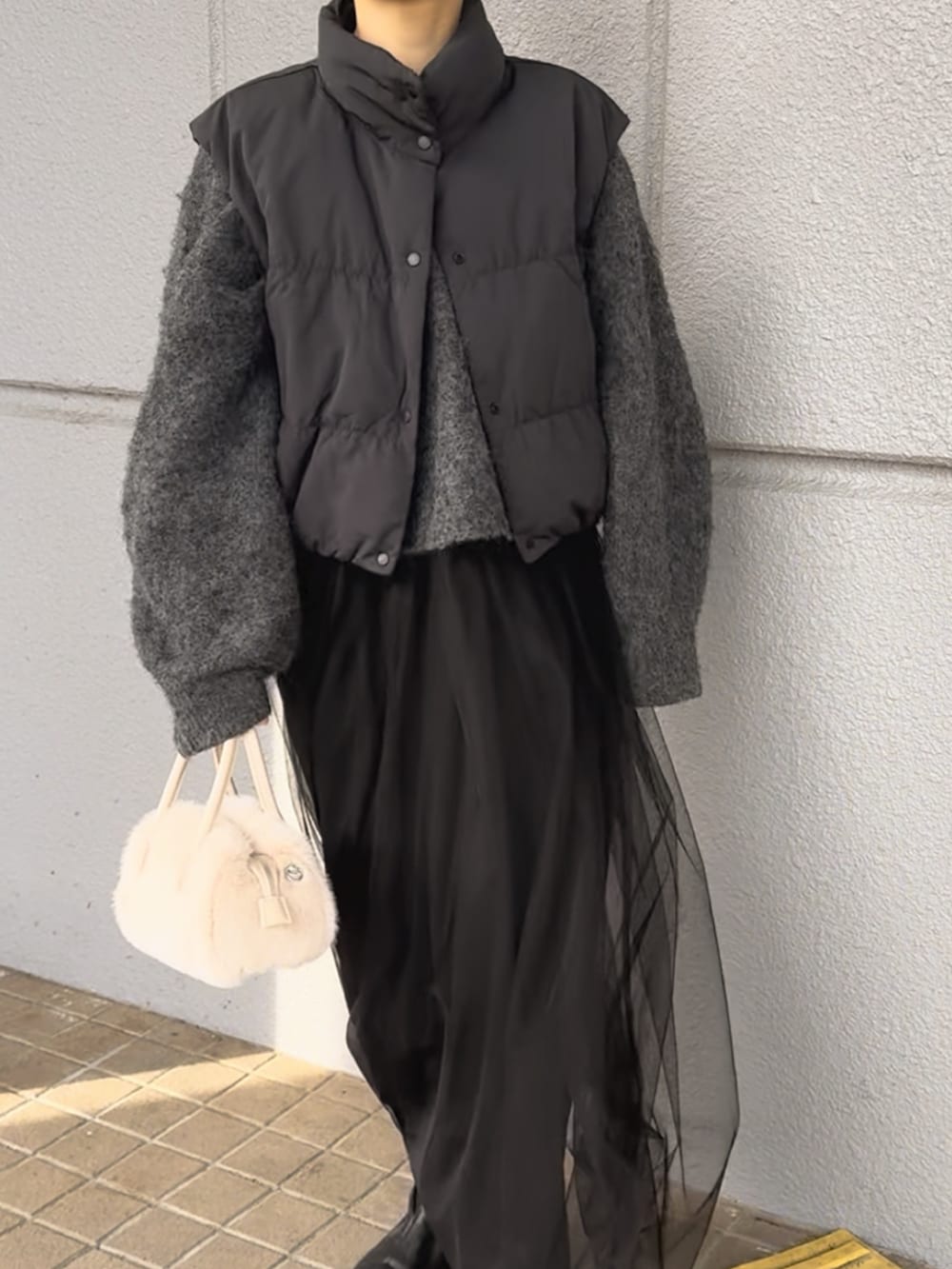 グレー系のワンピース、ブラック系のダウンベスト、ホワイト系のバッグを着用したレディースの冬コーディネートの3枚目の写真