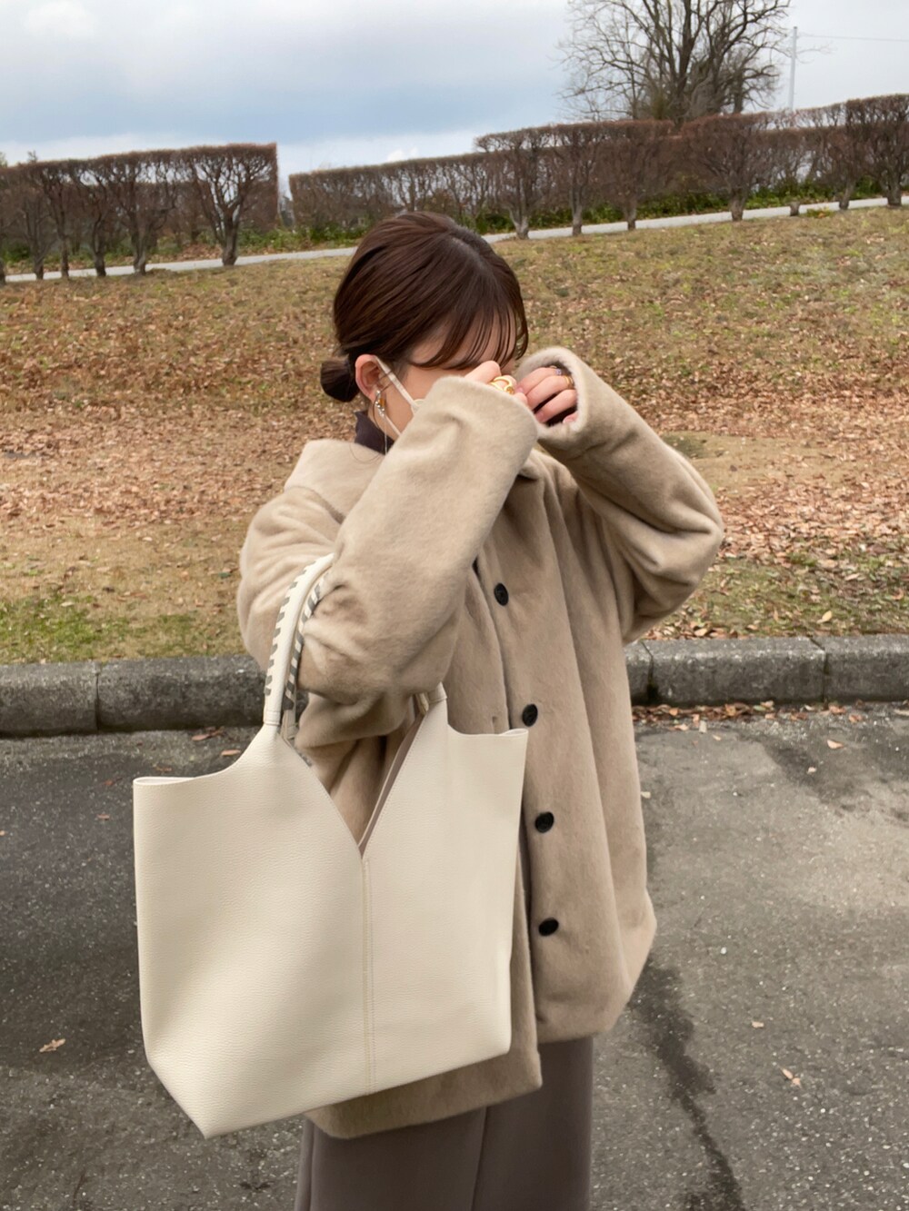 ブラウン系のワンピース、ホワイト系のトートバッグ、ベージュ系のステンカラーコートを着用したレディースの冬コーディネートの5枚目の写真