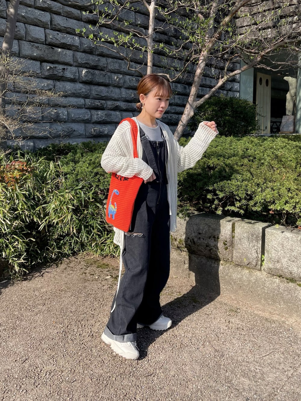 オレンジ系のトートバッグ、シルバー系のトップス、ホワイト系のカーディガン/ボレロを着用したレディースの春コーディネートの3枚目の写真