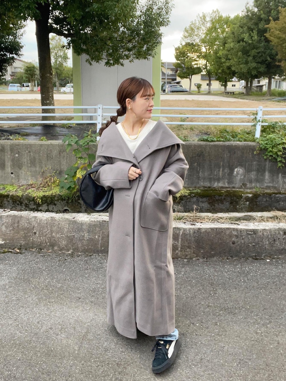 グレー系のトレンチコート、ホワイト系のニット/セーター、ブラック系のハンドバッグを着用したレディースの秋コーディネートの3枚目の写真