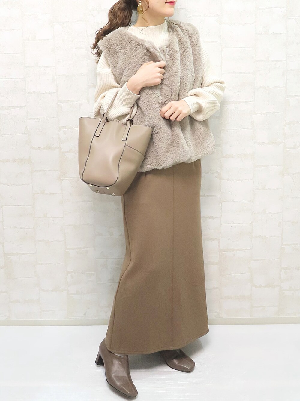 ベージュ系のその他アウター、ホワイト系のニット/セーター、ブラウン系のスカートを着用したレディースの冬コーディネートの2枚目の写真