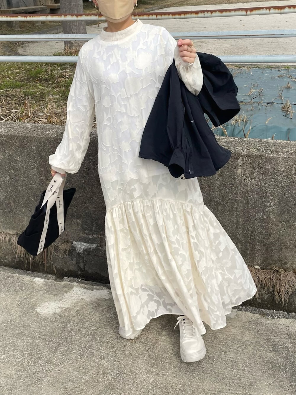 ホワイト系のドレス、ブラック系のトートバッグ、ブラック系のマウンテンパーカーを着用したレディースの冬コーディネートの3枚目の写真