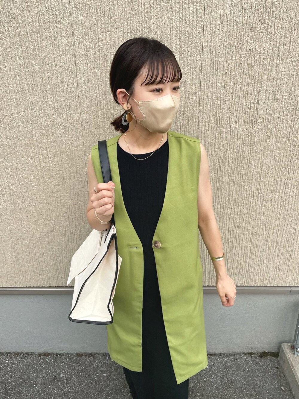 ホワイト系のトートバッグ、グリーン系のベスト、ブラック系のワンピースを着用したレディースの夏コーディネートの4枚目の写真