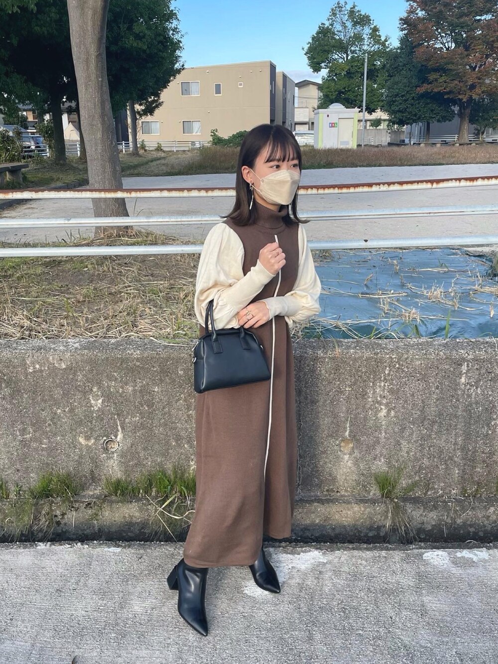 ブラウン系のワンピース、ブラック系のボストンバッグ、ブラック系のブーツを着用したレディースの秋コーディネートの2枚目の写真