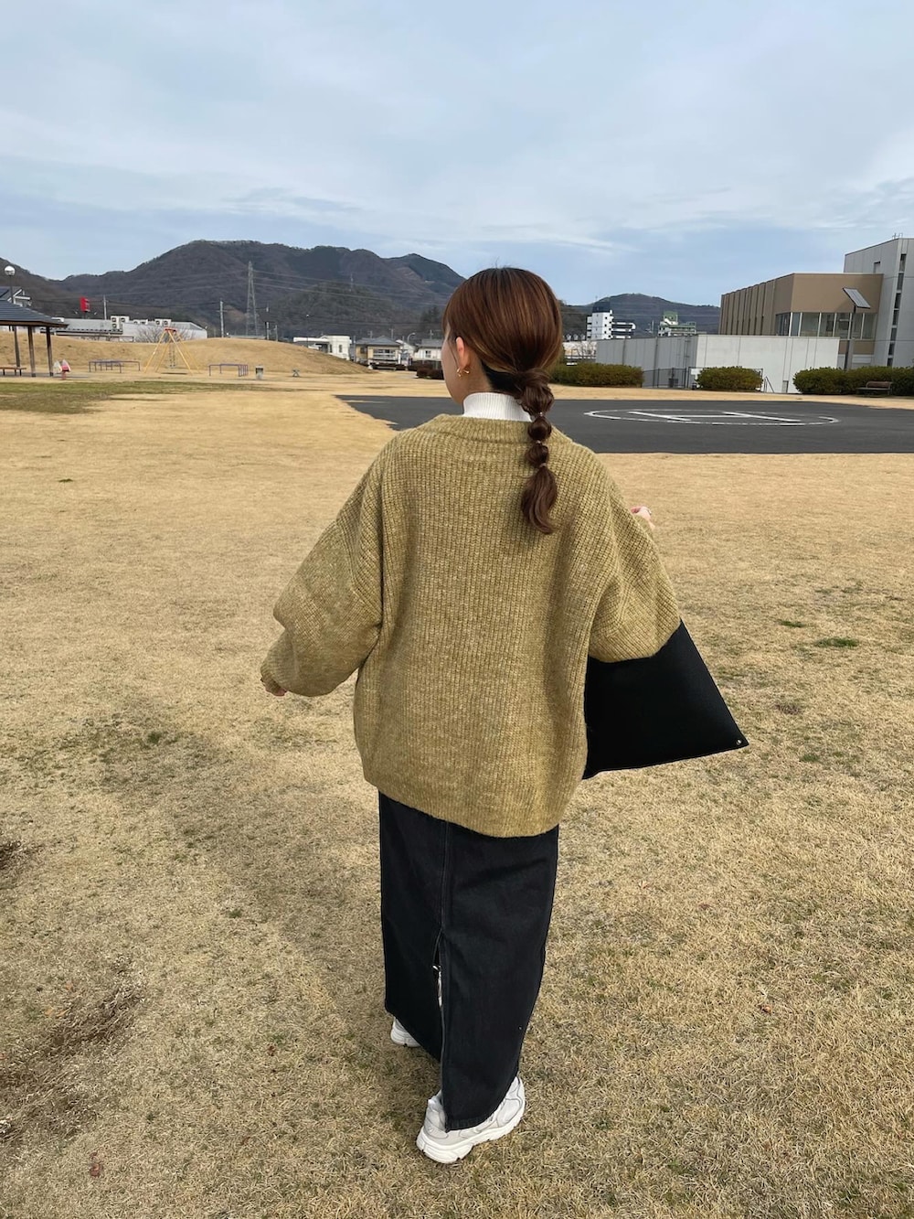 グリーン系のニット/セーター、ブラック系のデニムスカート、ブラック系のトートバッグを着用したレディースの冬コーディネートの3枚目の写真