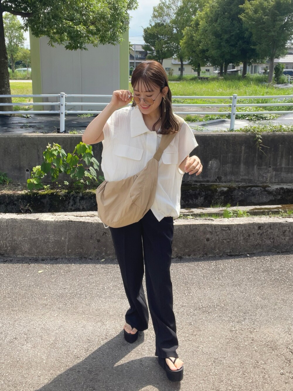 ベージュ系のショルダーバッグ、ブラック系のパンツ、ブラック系のサンダルを着用したレディースの夏コーディネートの2枚目の写真