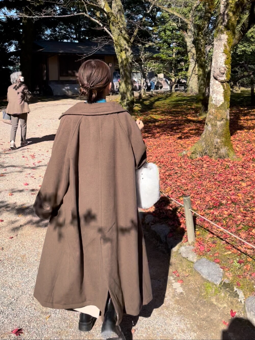 ブラウン系のステンカラーコート、ブルー系のニット/セーター、ベージュ系のスカートを着用したレディースの秋コーディネートの3枚目の写真