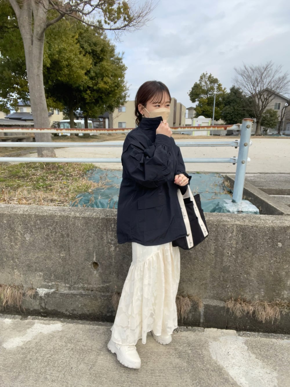 ホワイト系のドレス、ブラック系のトートバッグ、ブラック系のマウンテンパーカーを着用したレディースの冬コーディネートの5枚目の写真