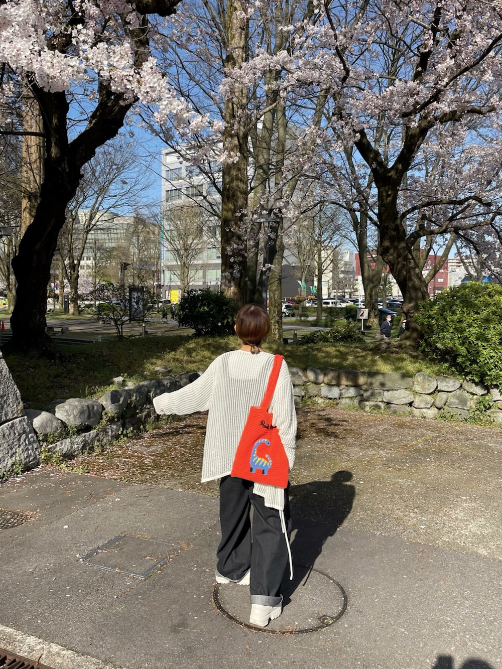 オレンジ系のトートバッグ、シルバー系のトップス、ホワイト系のカーディガン/ボレロを着用したレディースの春コーディネートの4枚目の写真