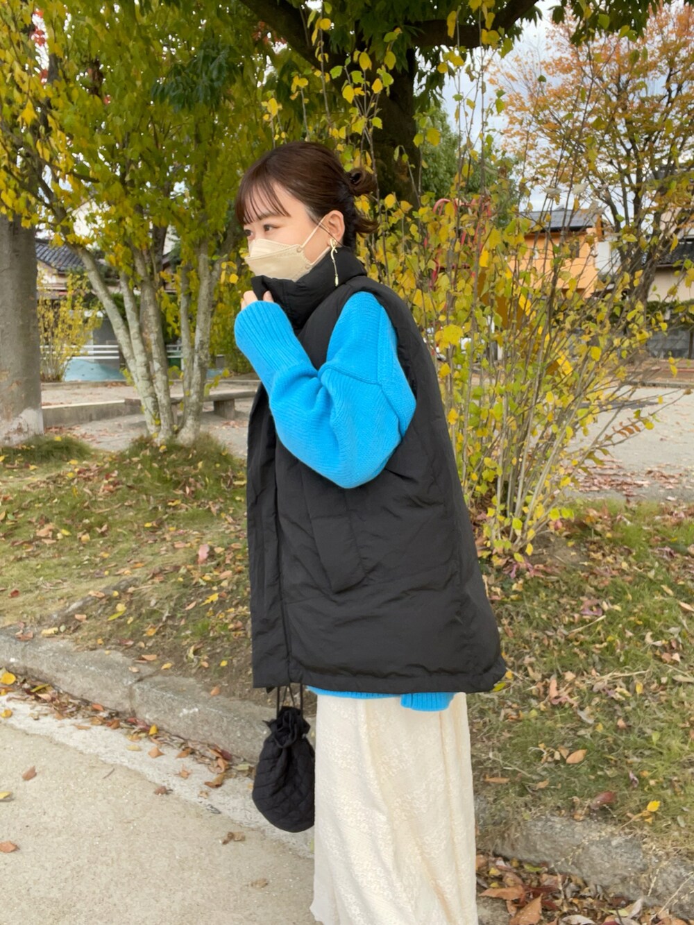 ベージュ系のスカート、ブルー系のカーディガン/ボレロ、ブラック系のダウンベストを着用したレディースの秋コーディネートの4枚目の写真