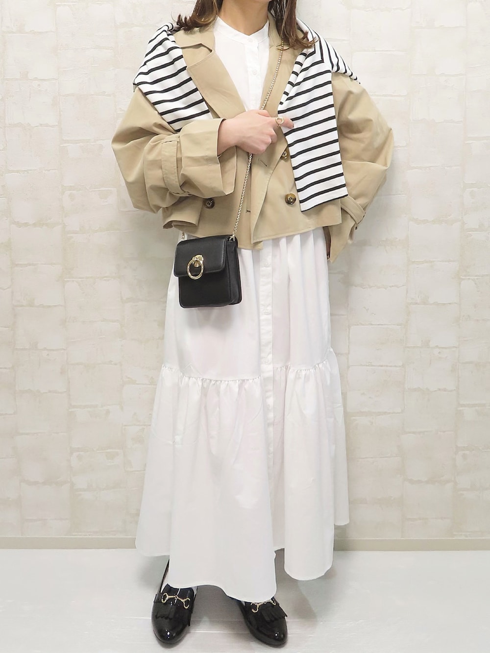 ベージュ系のトレンチコート、ホワイト系のワンピース/ドレス、ブラック系のショルダーバッグを着用したレディースの春コーディネートの3枚目の写真