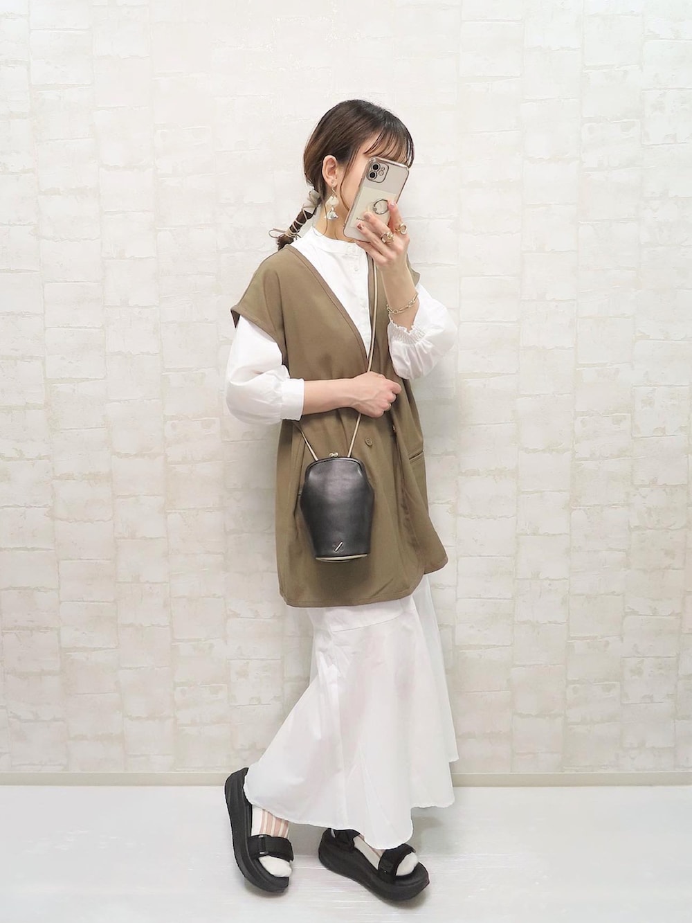 ホワイト系のワンピース、ブラウン系のベスト、ブラック系のショルダーバッグを着用したレディースの春コーディネートの4枚目の写真