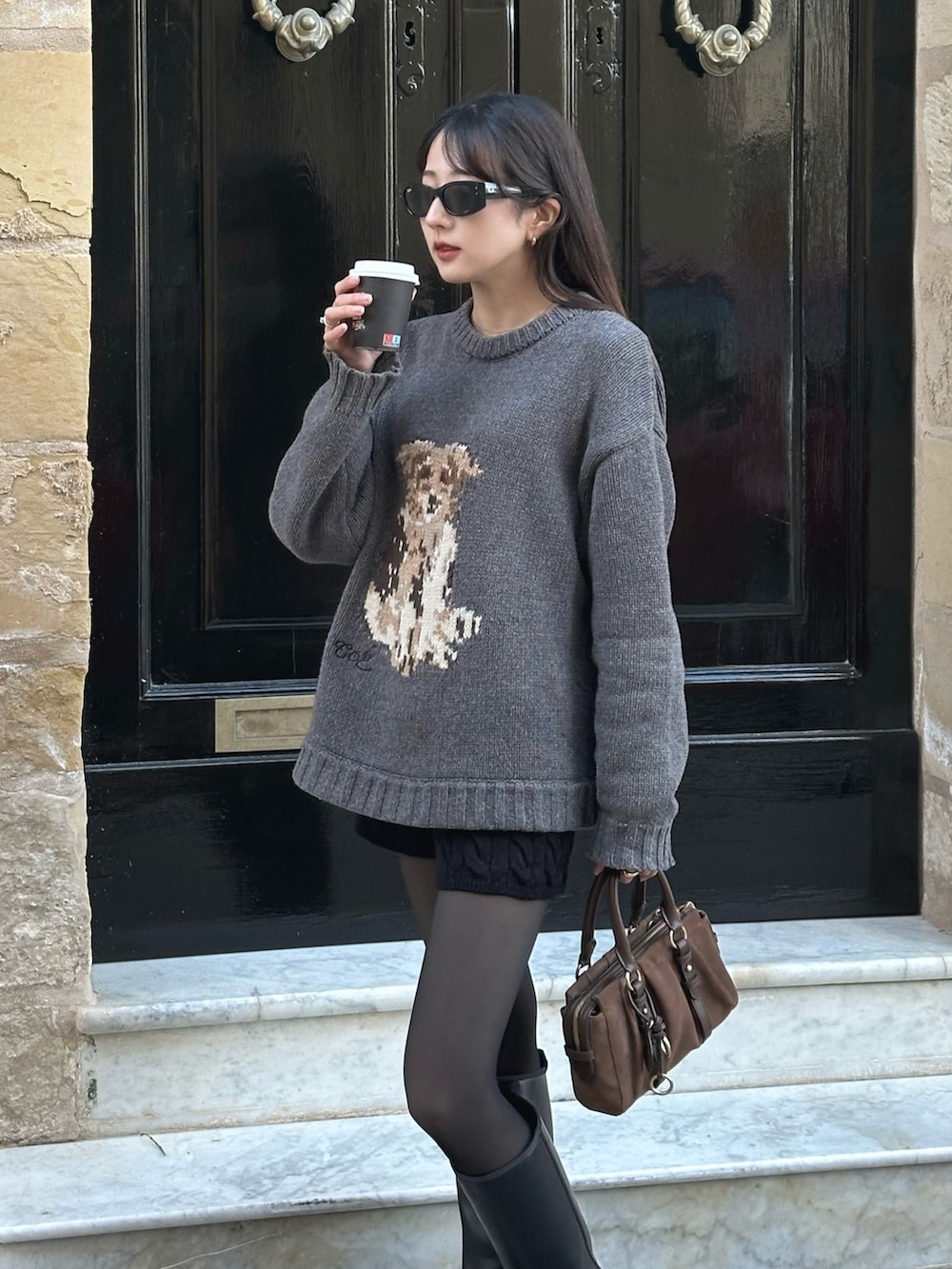 ブラウン系のトートバッグ、グレー系のニット/セーター、ブラック系のその他パンツを着用したレディースの春コーディネートの2枚目の写真