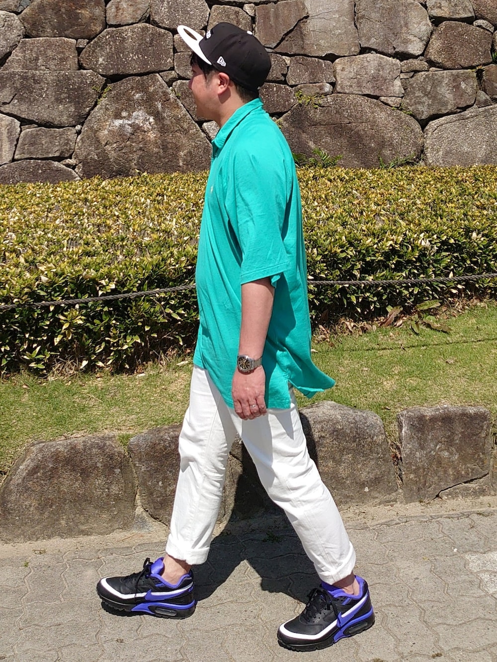 グリーン系のポロシャツ、ホワイト系のデニムパンツ、ブラック系のスニーカーを着用したメンズの春コーディネートの3枚目の写真