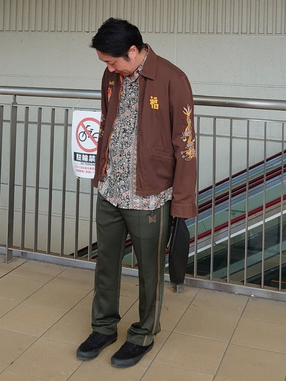 ブラウン系のミリタリージャケット、グリーン系のシャツ/ブラウス、ブラック系のクラッチバッグを着用したメンズの秋コーディネートの2枚目の写真