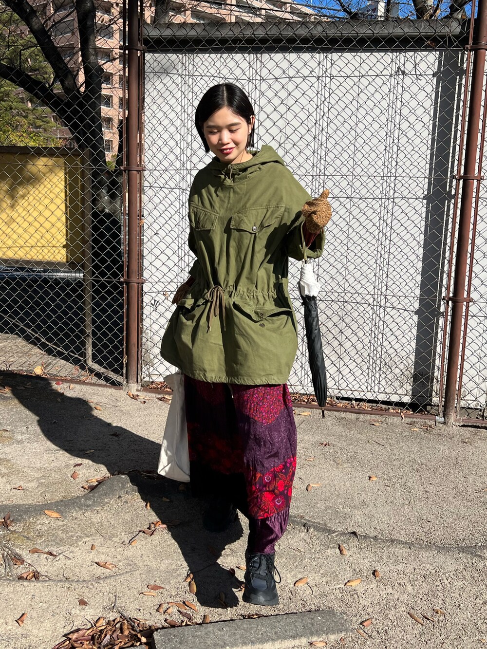 グリーン系のミリタリージャケット、レッド系のスカート、ブラック系のスニーカーを着用したレディースの冬コーディネートの2枚目の写真