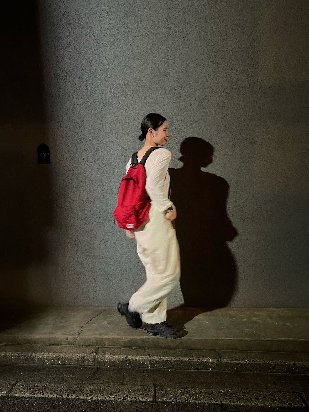 レッド系のバックパック/リュック、ブラック系のスニーカー、ベージュ系のパンツを着用したレディースの春コーディネートの2枚目の写真