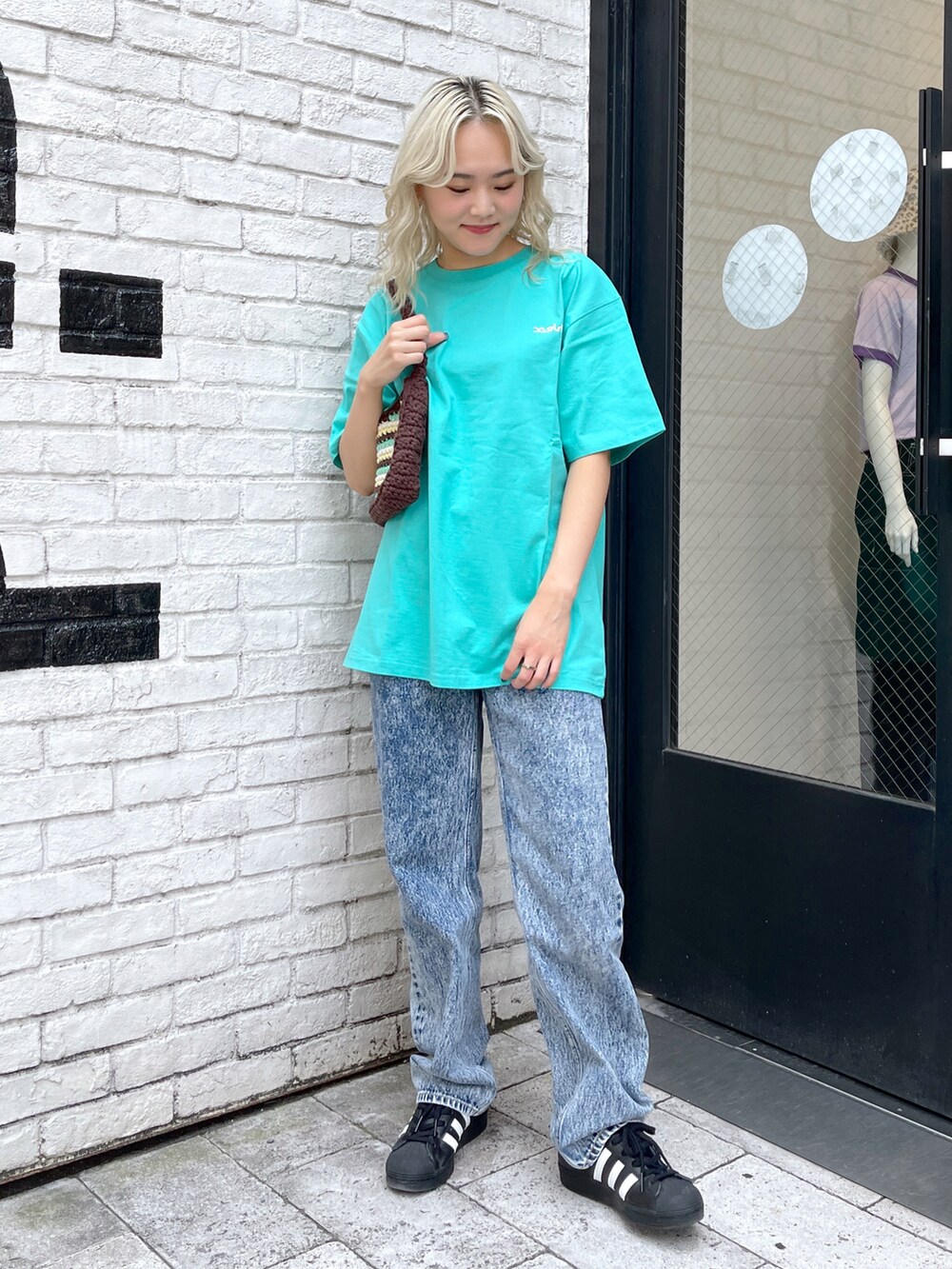 オレンジ系のハンドバッグ、グリーン系のTシャツ/カットソー、ブルー系のデニムパンツを着用したレディースの夏コーディネートの2枚目の写真