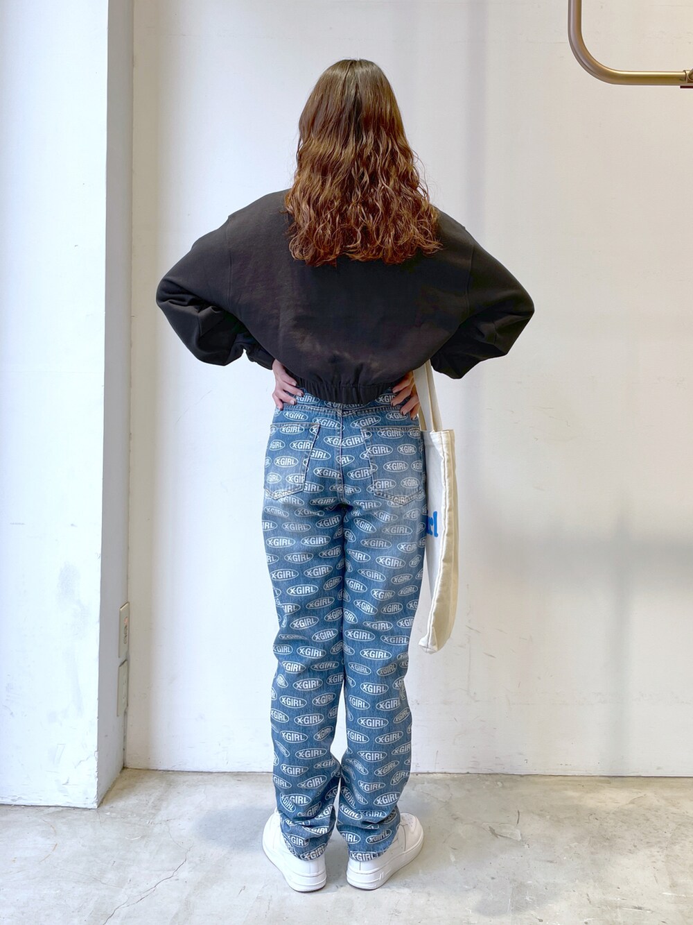 ブラック系のスウェット、ブルー系のデニムパンツ、ホワイト系のトートバッグを着用したレディースの春コーディネートの2枚目の写真