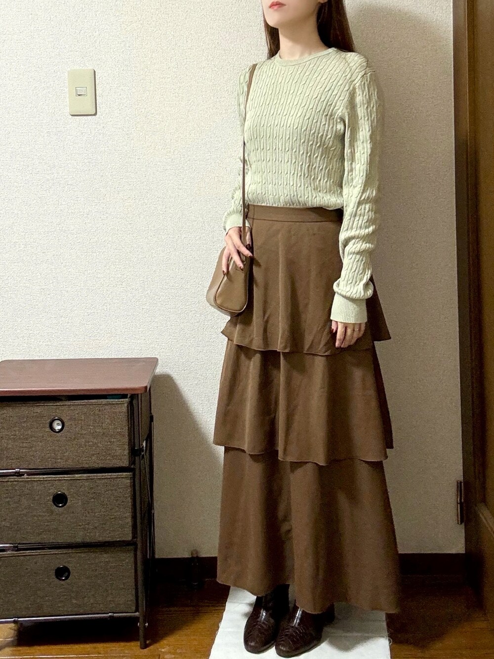 グリーン系のニット/セーター、ブラウン系のスカート、ブラウン系のブーツを着用したレディースの秋コーディネートの2枚目の写真