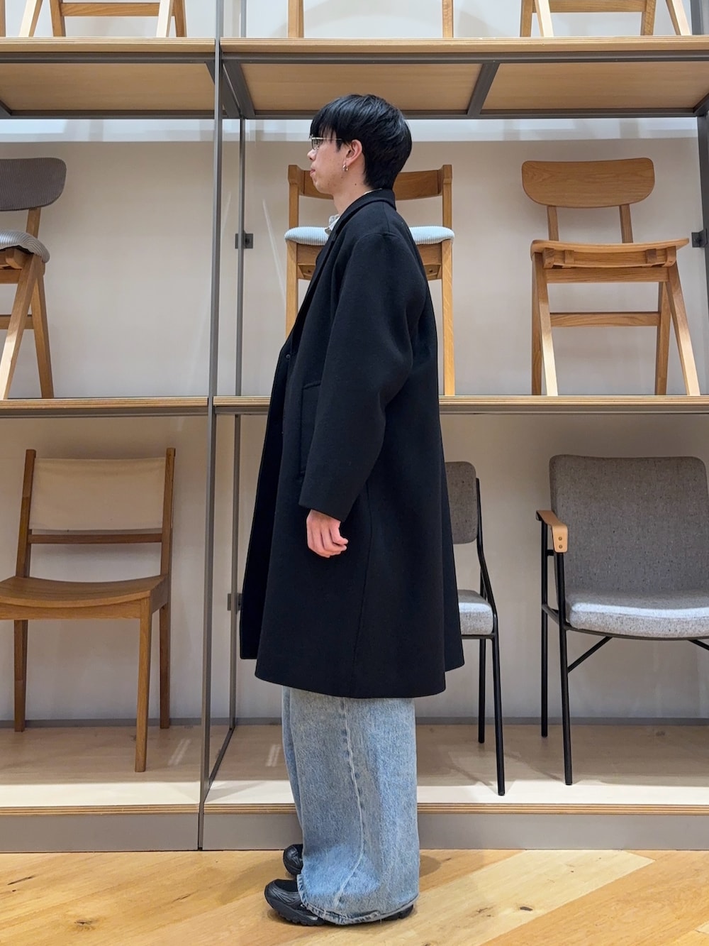 ブラック系のチェスターコート、ブラック系のニット/セーター、ブルー系のデニムパンツを着用したメンズの冬コーディネートの2枚目の写真