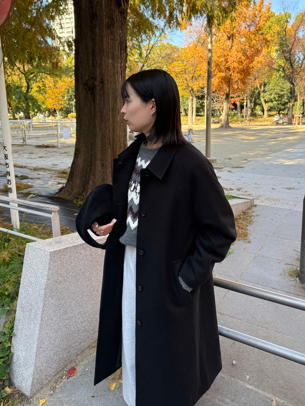グレー系のパンツ、ブラック系のステンカラーコート、グレー系のニット/セーターを着用したレディースの冬コーディネートの3枚目の写真
