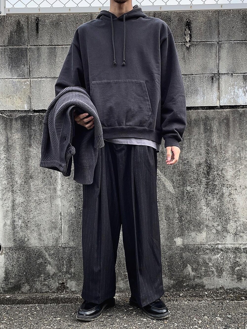 ブラック系のスラックス、ブラック系のカーディガン/ボレロ、グレー系のTシャツ/カットソーを着用したメンズの冬コーディネートの2枚目の写真