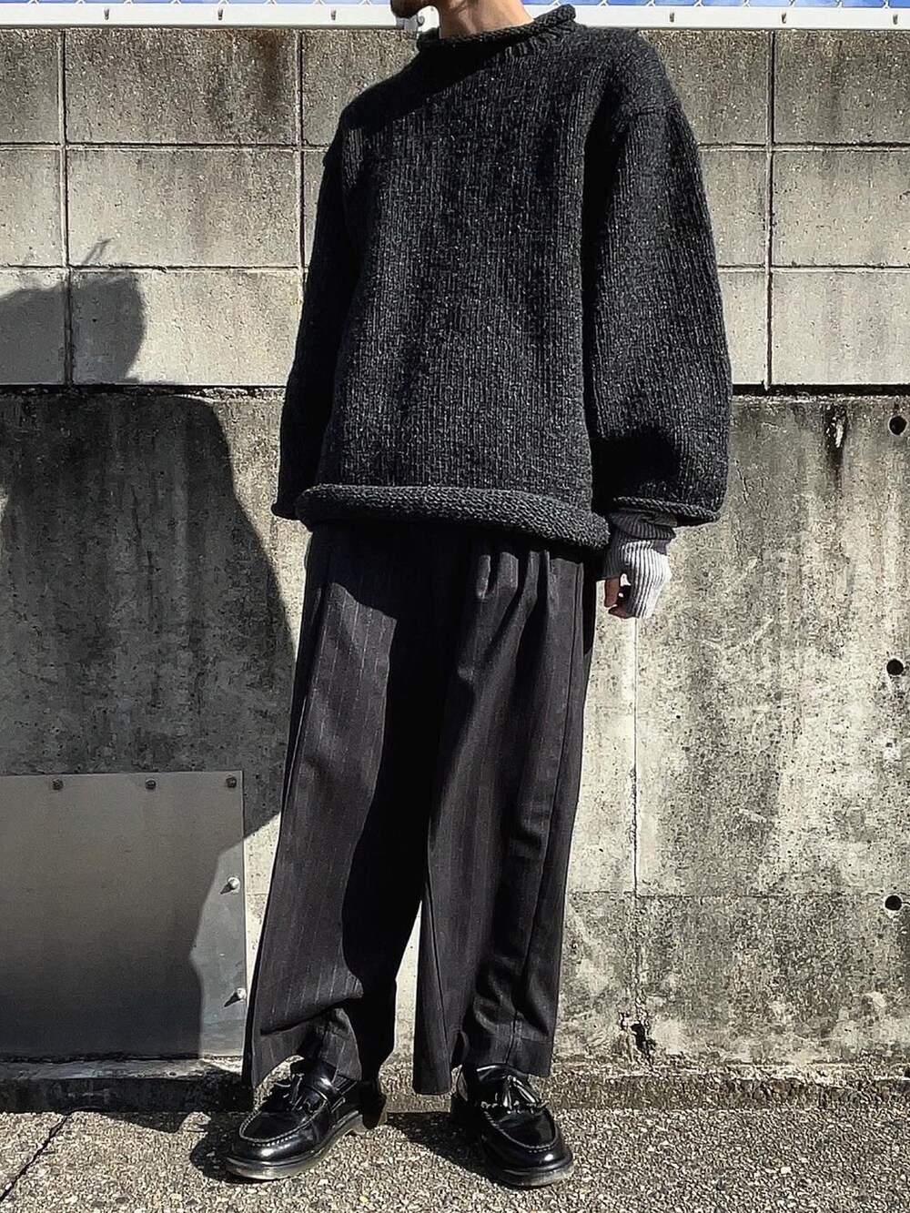 グレー系のニット/セーター、ブラック系のスラックス、ブラック系のローファーを着用したメンズの冬コーディネートの2枚目の写真
