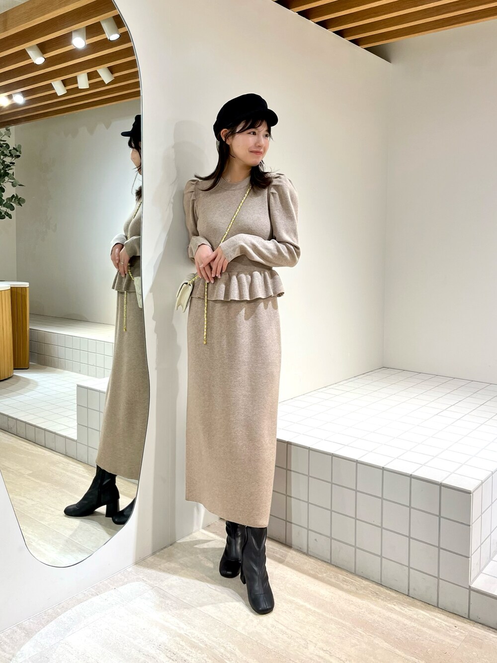 ベージュ系のワンピース、ホワイト系のショルダーバッグ、ブラック系のブーツを着用したレディースの冬コーディネートの2枚目の写真