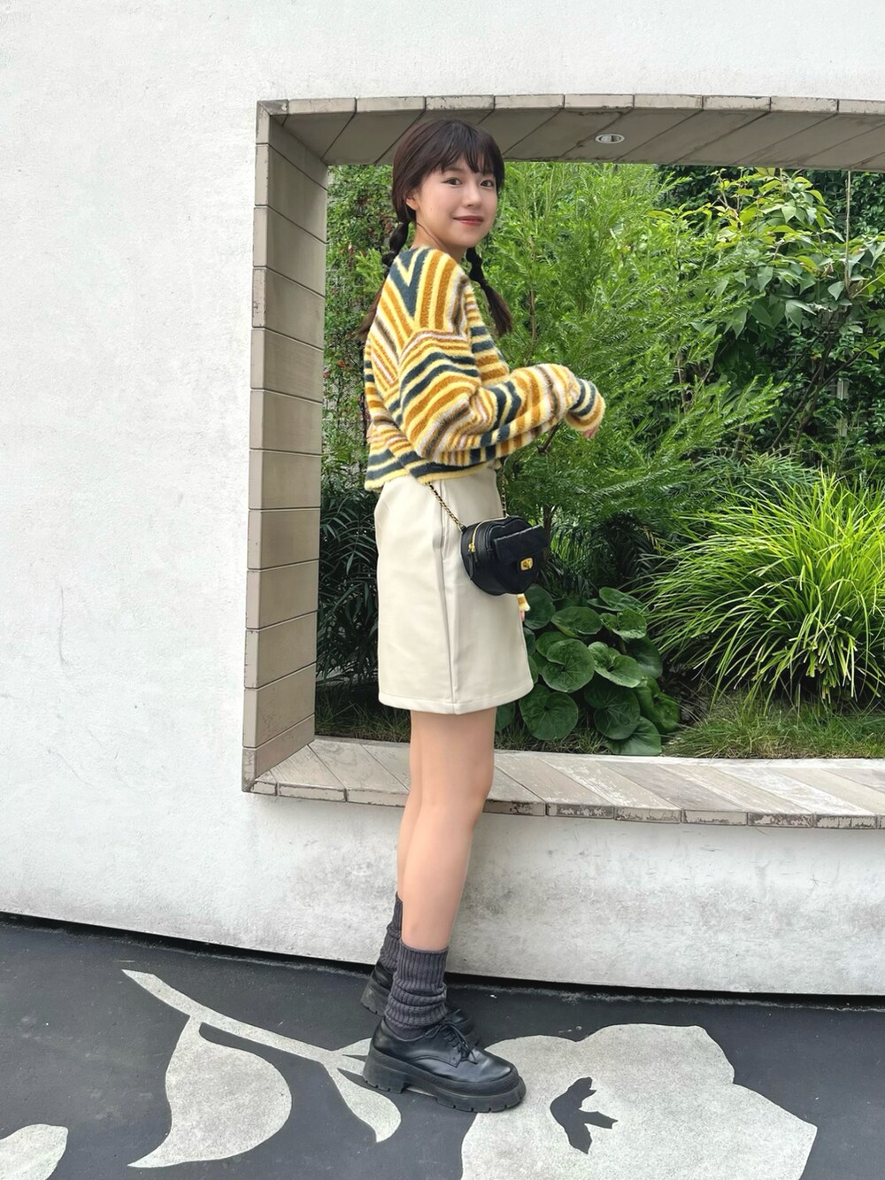 イエロー系のニット/セーター、ホワイト系のスカート、ブラック系のショルダーバッグを着用したレディースの秋コーディネートの2枚目の写真