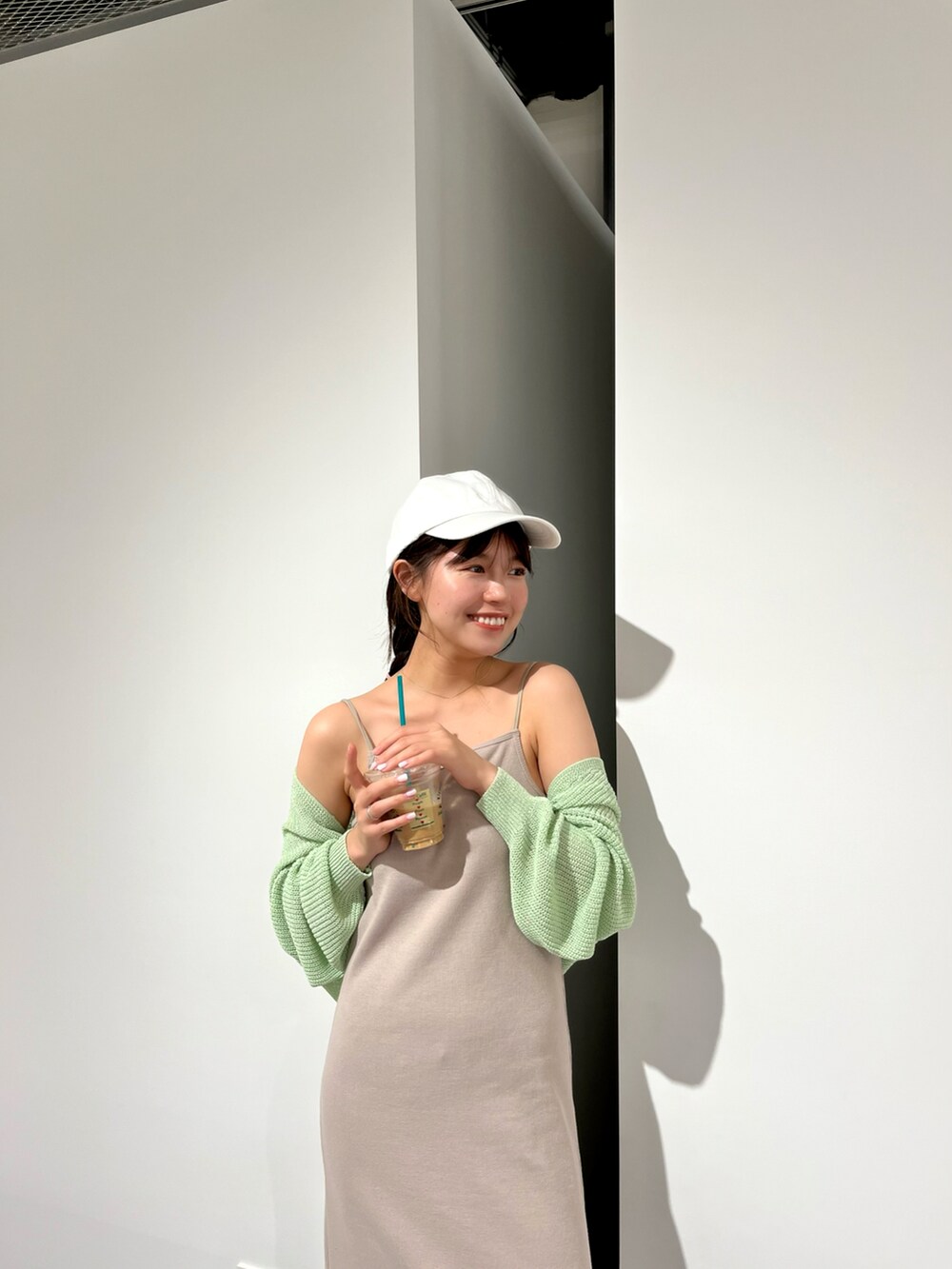 ベージュ系のワンピース、グリーン系のカーディガン/ボレロ、ホワイト系のスニーカーを着用したレディースの春コーディネートの2枚目の写真