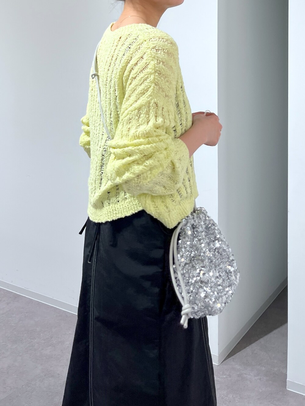 イエロー系のニット/セーター、ブラック系のワンピース、シルバー系のハンドバッグを着用したレディースの春コーディネートの2枚目の写真