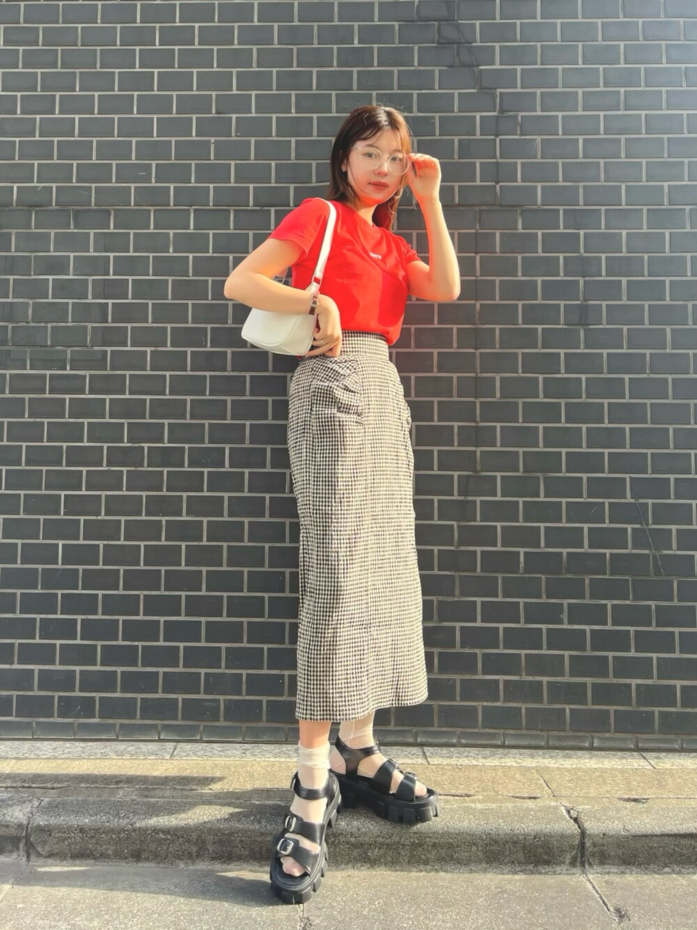 レッド系のTシャツ/カットソー、ブラック系のスカート、ホワイト系のショルダーバッグを着用したレディースの春コーディネートの2枚目の写真