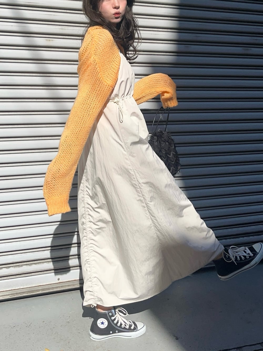 オレンジ系のニット/セーター、ホワイト系のワンピースを着用したレディースの春コーディネートの2枚目の写真
