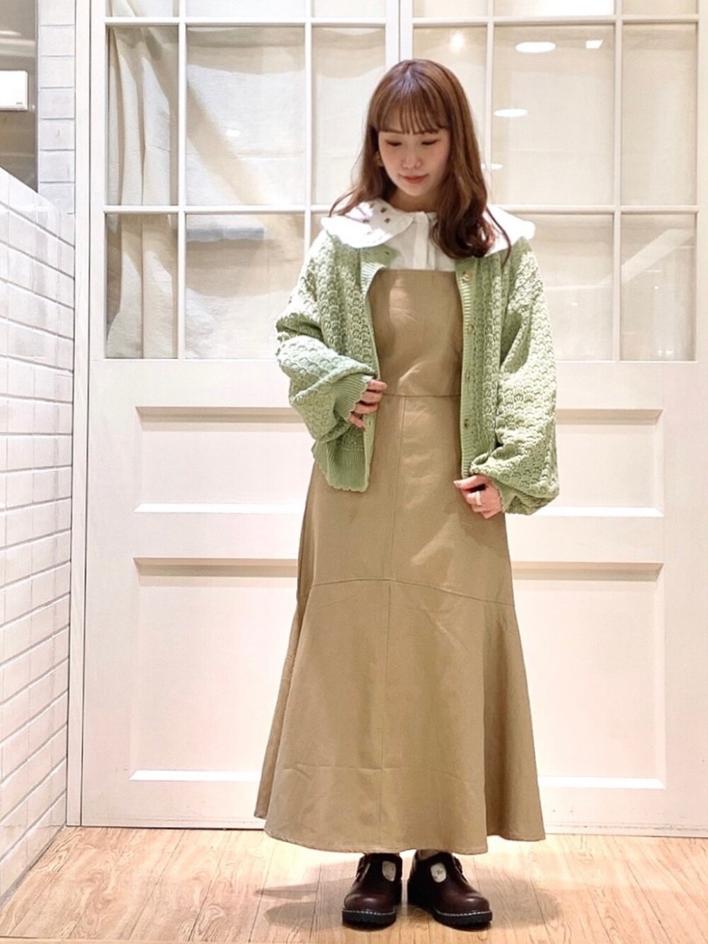 ベージュ系のジャンパースカート、ホワイト系のシャツ/ブラウス、グリーン系のカーディガン/ボレロを着用したレディースの春コーディネートの2枚目の写真