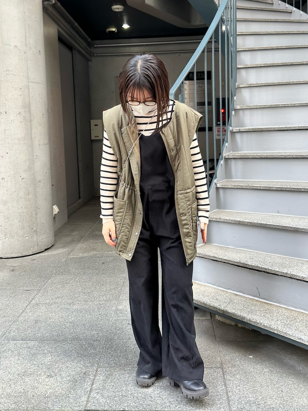 グリーン系のベスト、ブラック系のサロペット/オーバーオール、ブラック系のブーツを着用したレディースの冬コーディネートの5枚目の写真