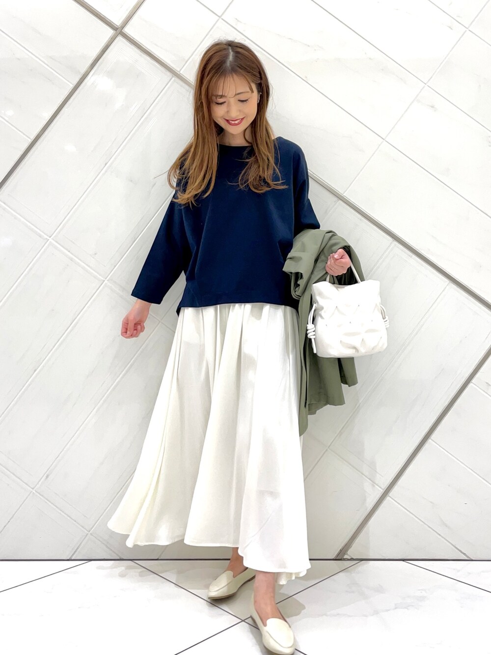 グリーン系のポンチョ、ホワイト系のスカート、ブルー系のTシャツ/カットソーを着用したレディースの春コーディネートの7枚目の写真