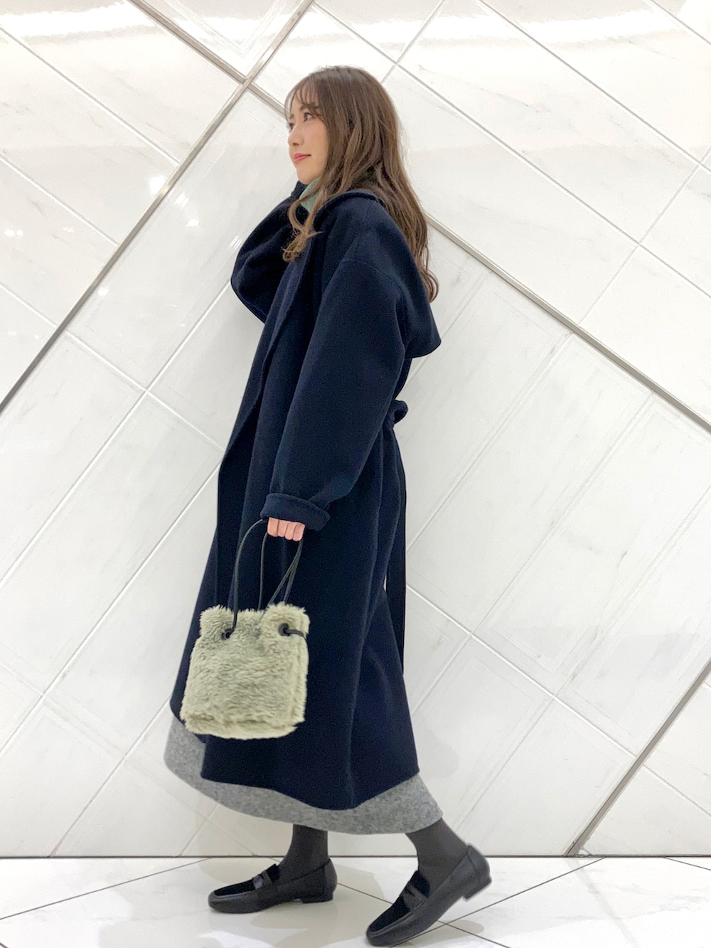 グリーン系のハンドバッグ、ブルー系のチェスターコート、ブラック系のローファーを着用したレディースの冬コーディネートの2枚目の写真