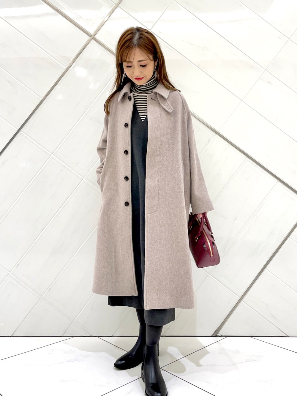 グレー系のステンカラーコート、ホワイト系のニット/セーター、グレー系のワンピースを着用したレディースの冬コーディネートの2枚目の写真