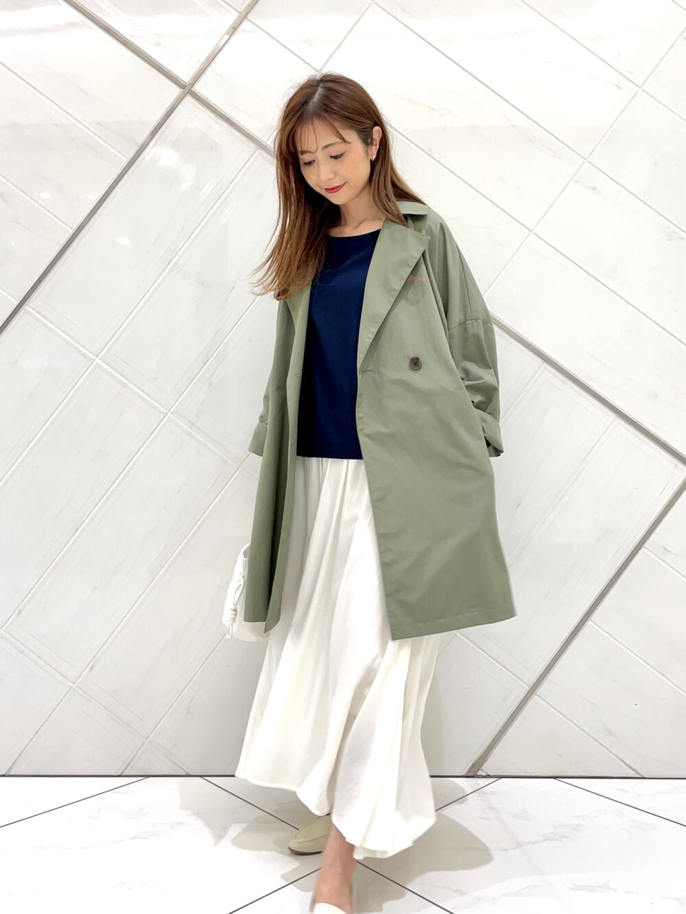 グリーン系のポンチョ、ホワイト系のスカート、ブルー系のTシャツ/カットソーを着用したレディースの春コーディネートの3枚目の写真