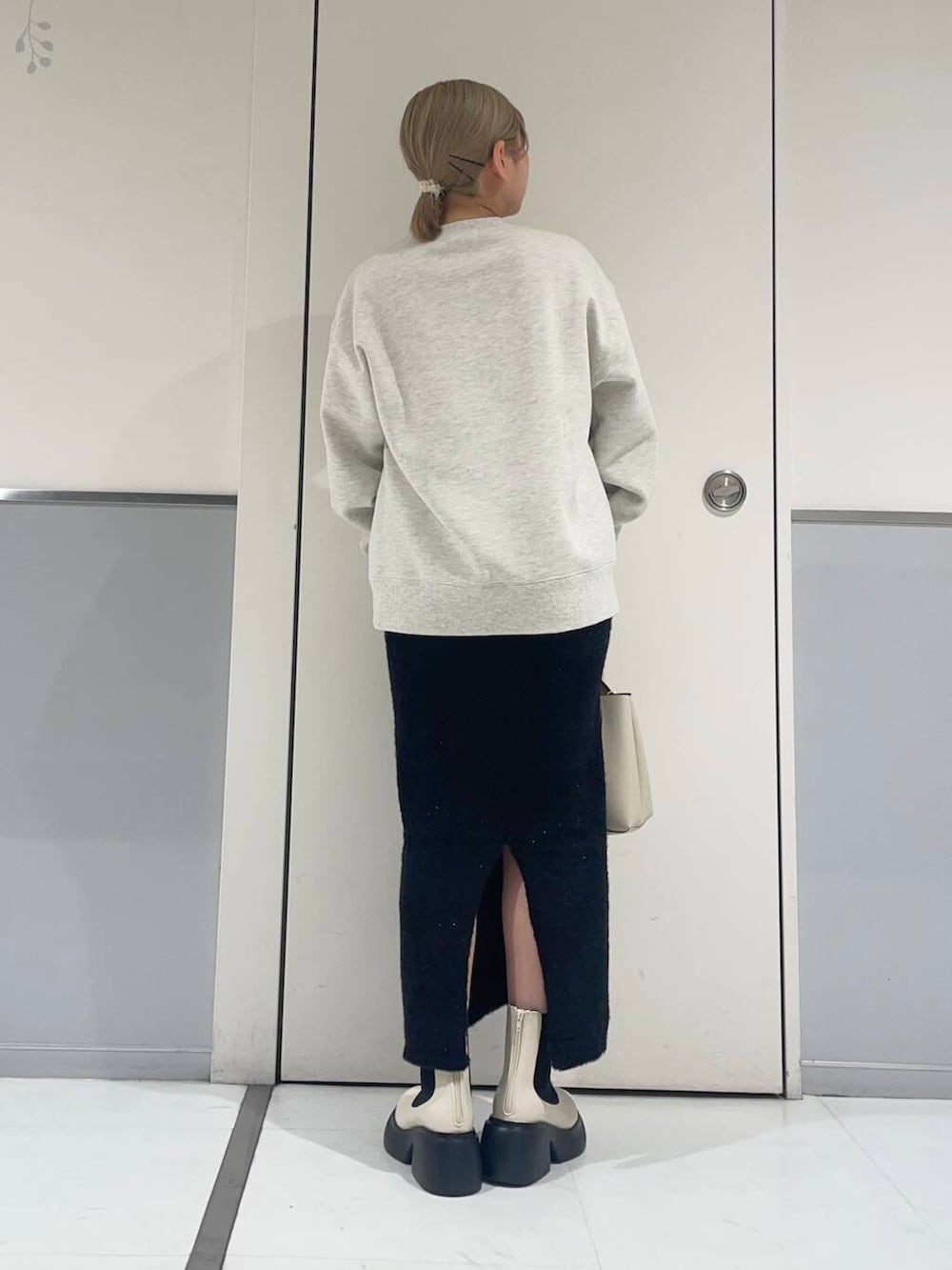 ホワイト系のトートバッグ、ホワイト系のブーツ、ブラック系のスカートを着用したレディースの秋コーディネートの2枚目の写真