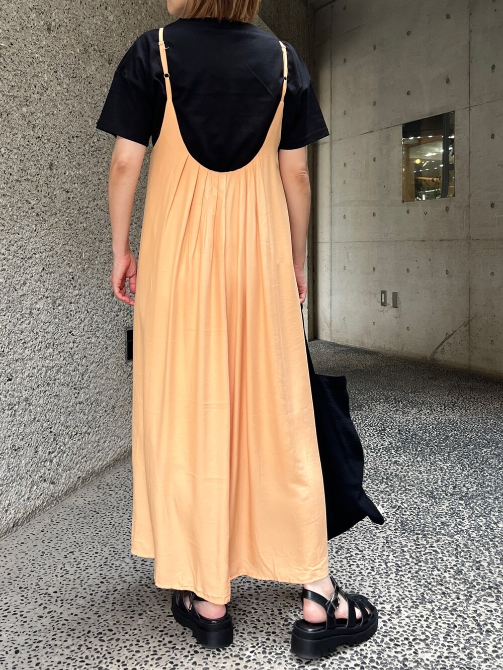 オレンジ系のワンピース、ブラック系のTシャツ/カットソー、ブラック系のトートバッグを着用したレディースの夏コーディネートの2枚目の写真