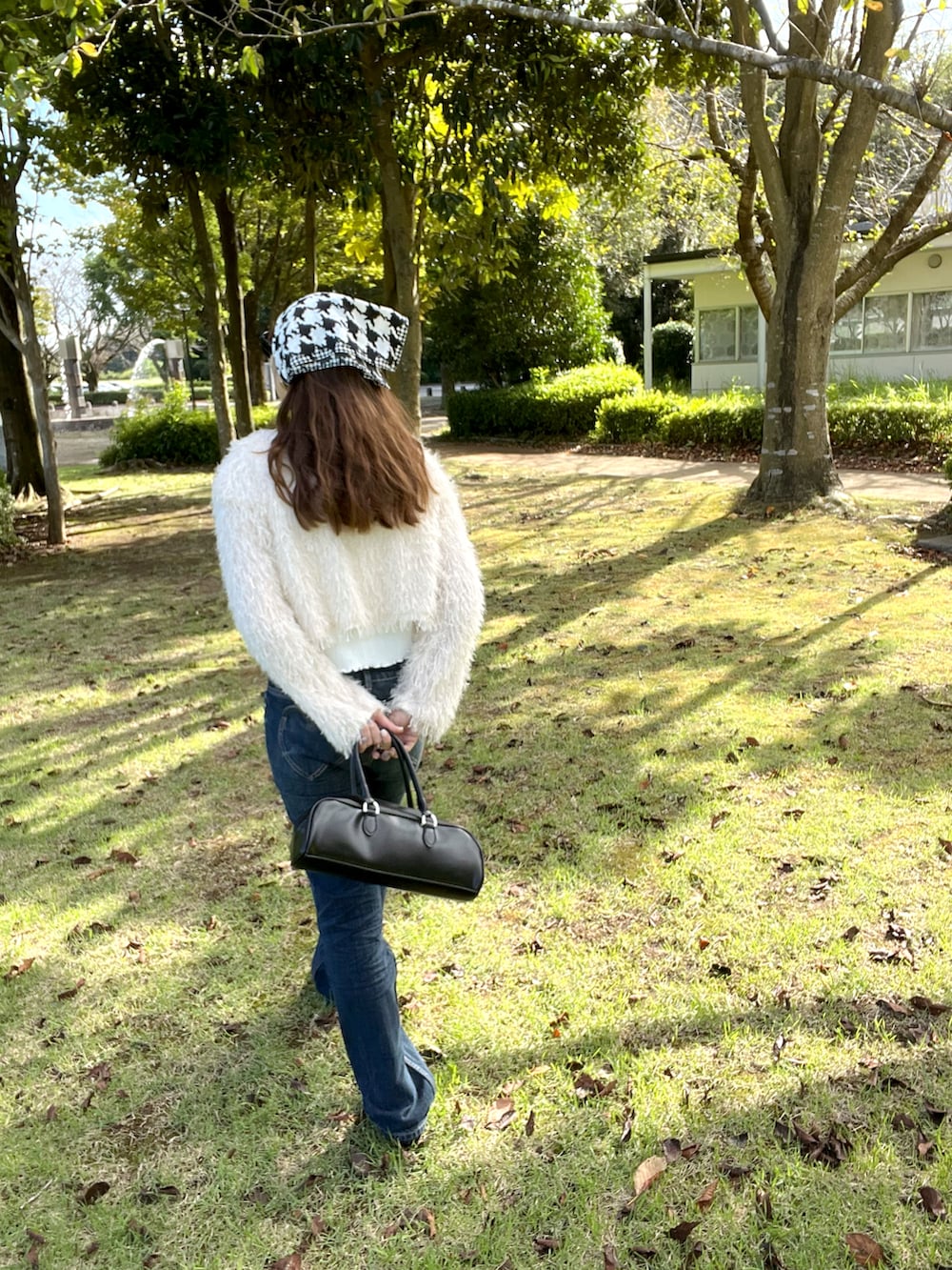 ブラック系のボストンバッグ、ホワイト系のカーディガン/ボレロ、ブルー系のデニムパンツを着用したレディースの秋コーディネートの3枚目の写真