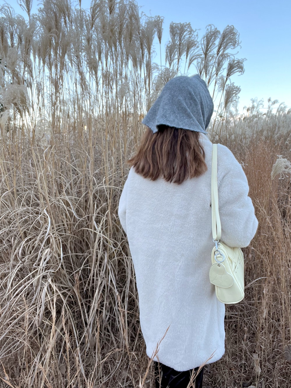 イエロー系のショルダーバッグ、ベージュ系のステンカラーコートを着用したレディースの冬コーディネートの3枚目の写真