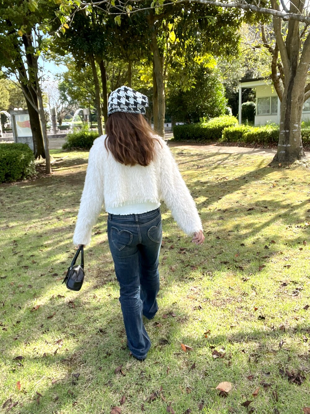 ブラック系のボストンバッグ、ホワイト系のカーディガン/ボレロ、ブルー系のデニムパンツを着用したレディースの秋コーディネートの2枚目の写真